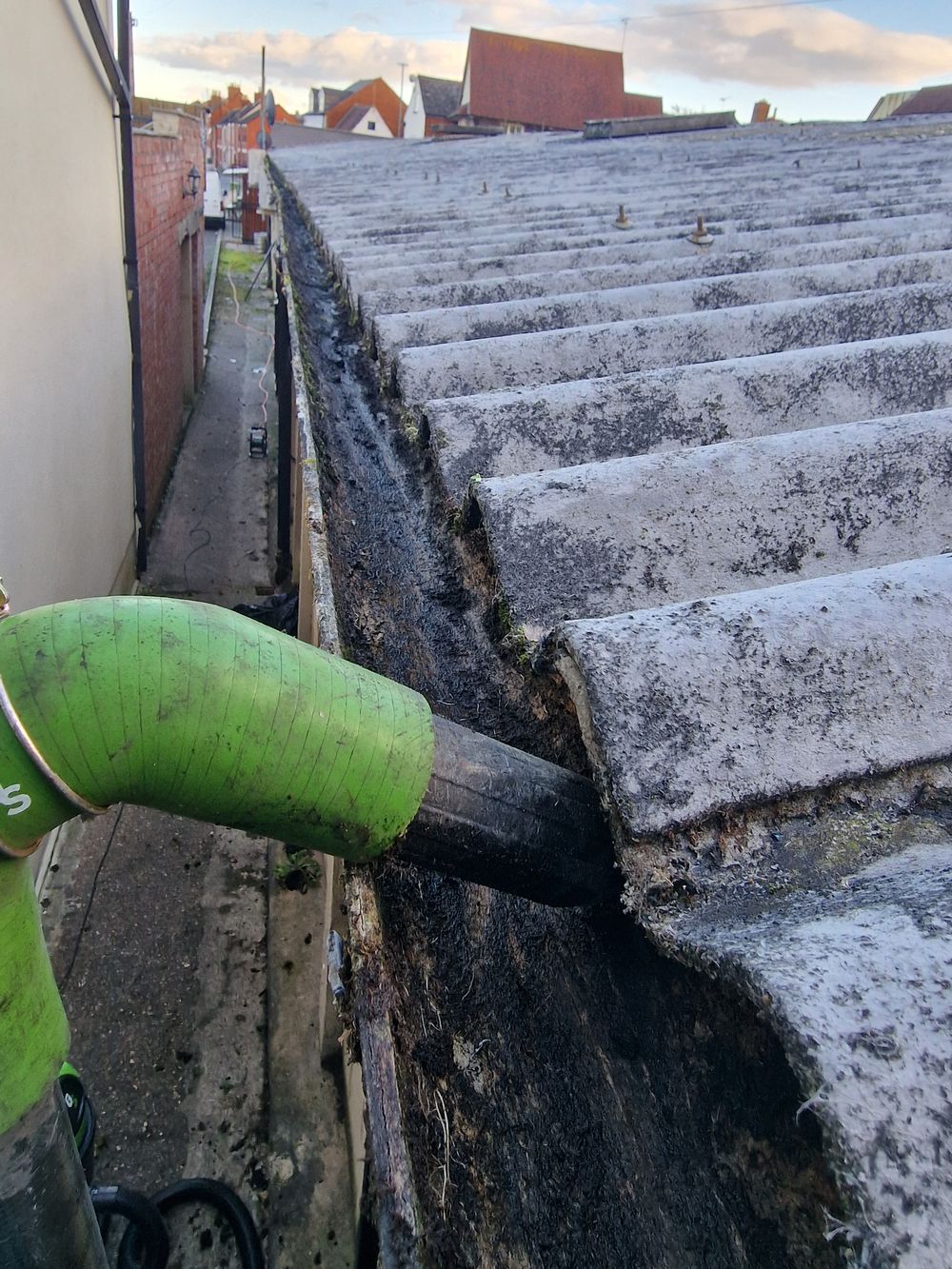 High-reach vacuum pulling moss out of a blocked gutter